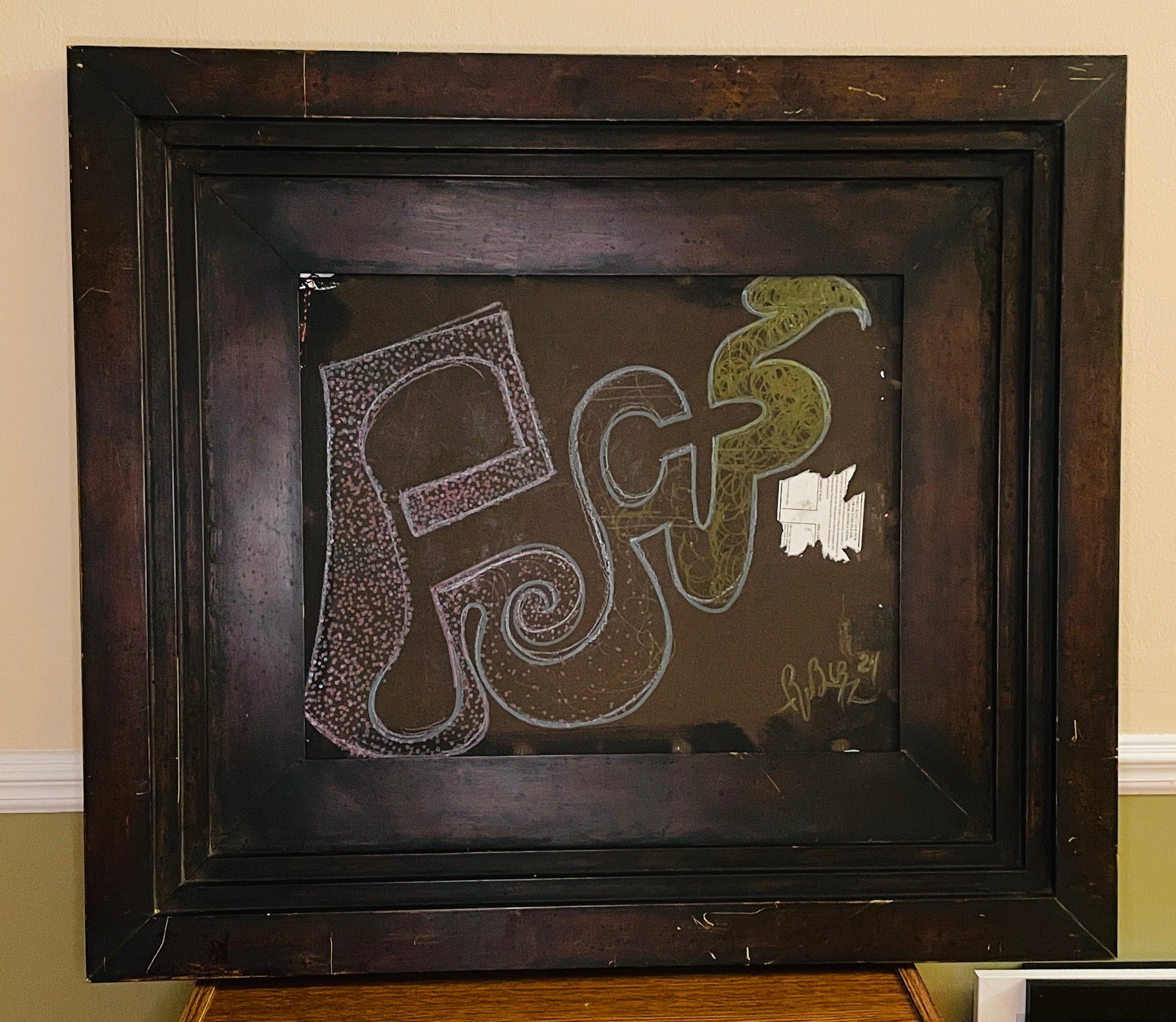 Abstract mixed-media assemblage in a deep, weathered dark wood frame. Pink, blue and green invented glyphs, dots, spirals and tangled lines appear on a brown field beside a torn fragment of printed paper.